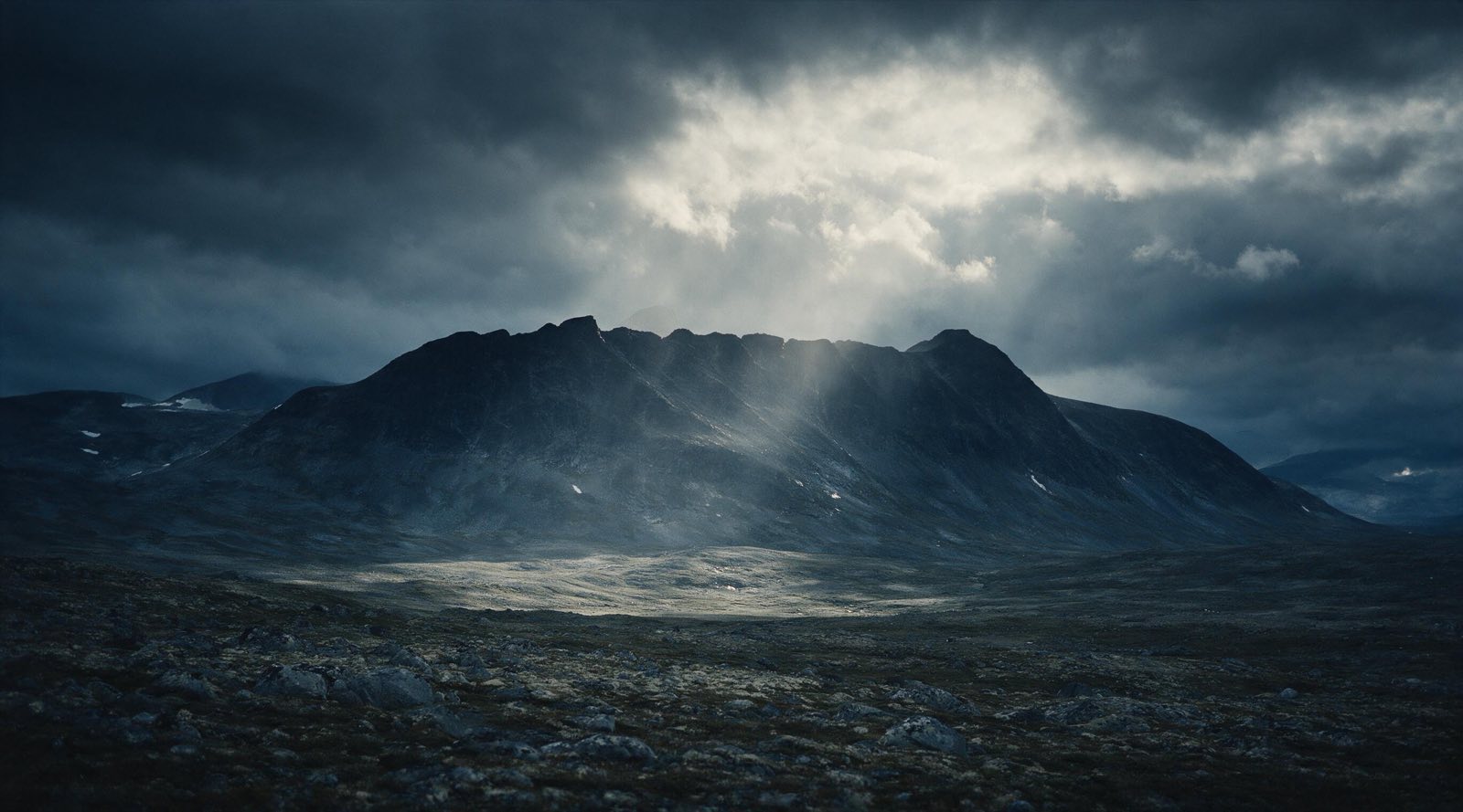 A dark mountain ridge under breaking storm light