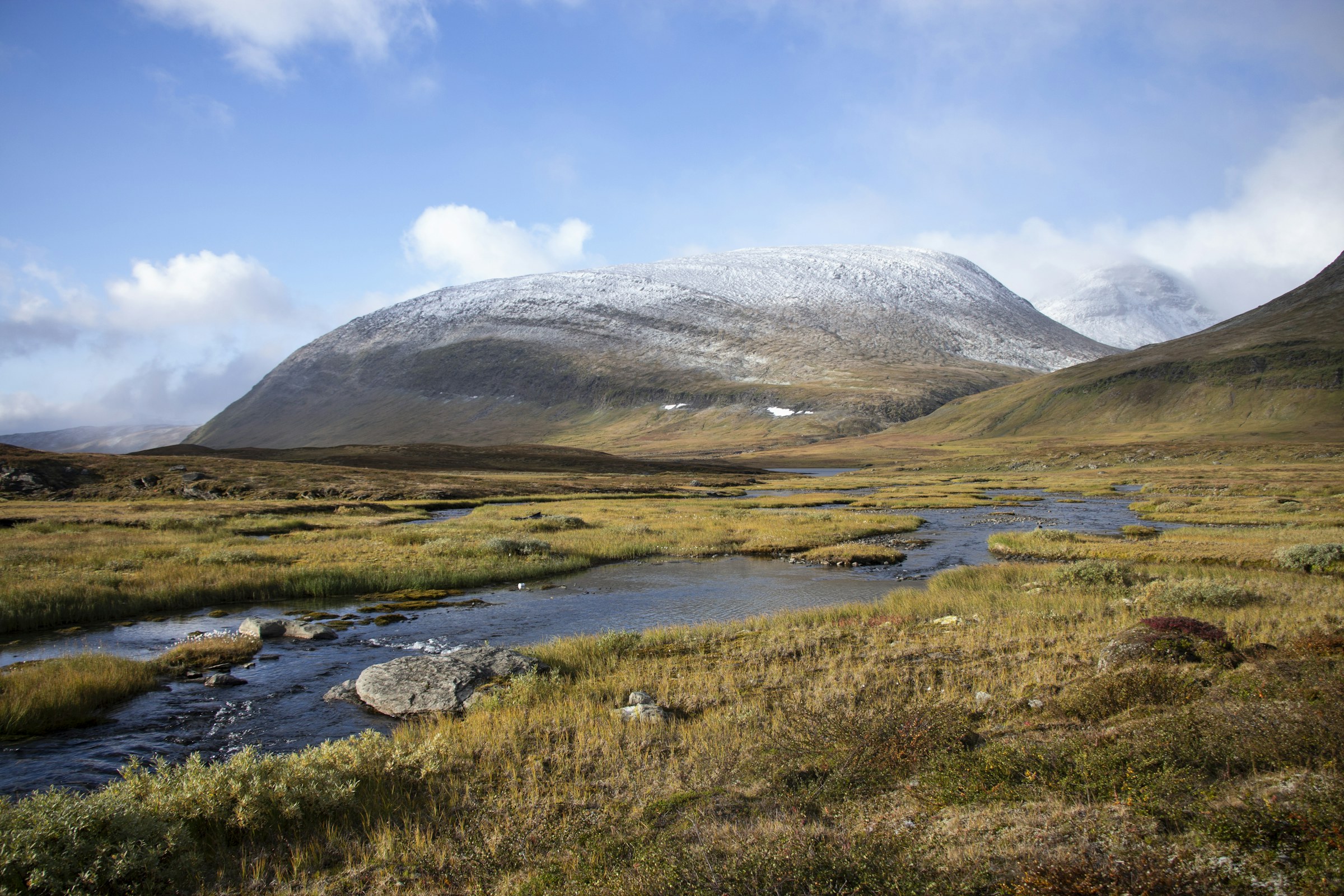 A stream through russet autumn ground at Abisko, snow-capped mountain behind