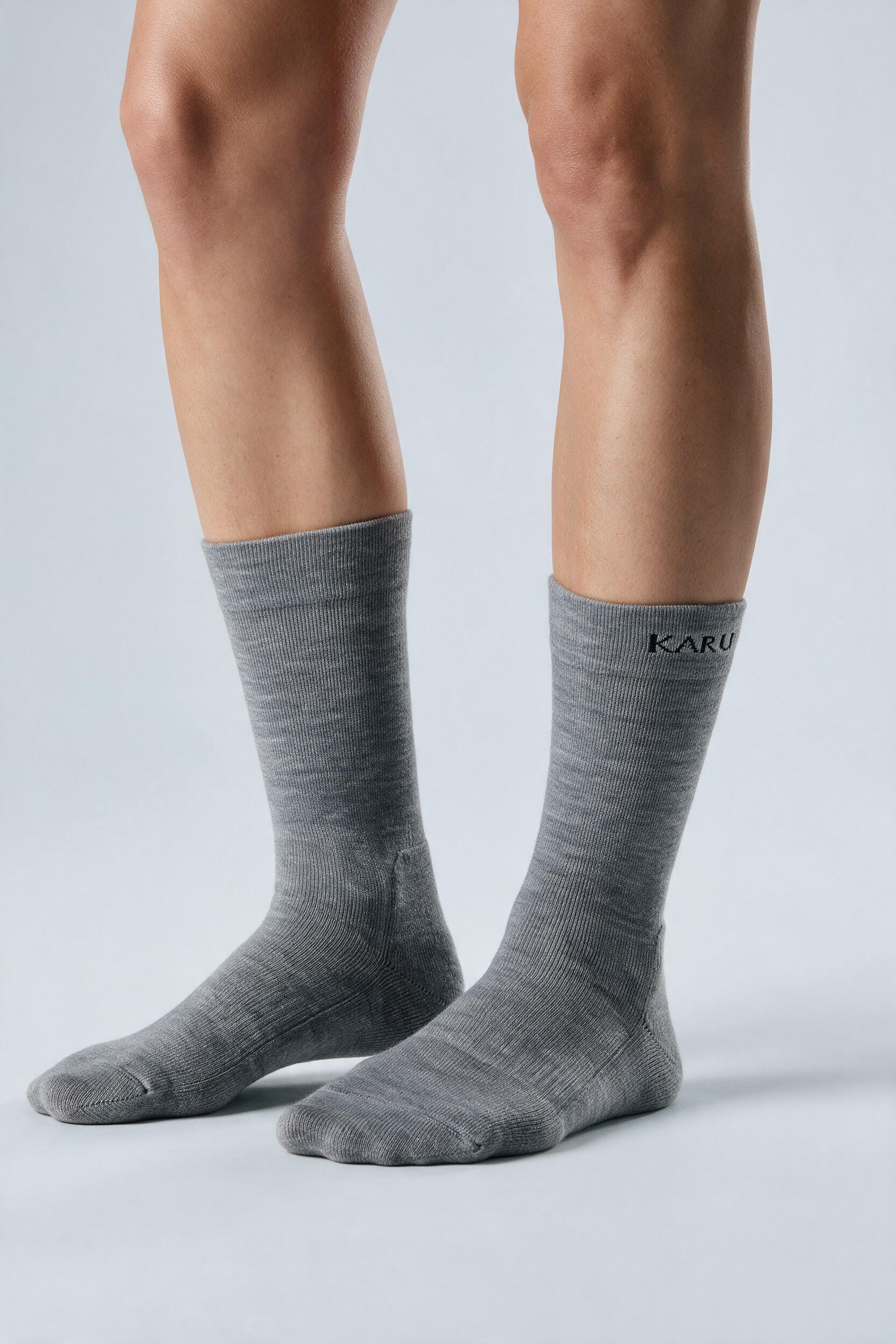 Tjäktja Sock pair in ash, worn on the feet, studio product shot on a seamless neutral ground